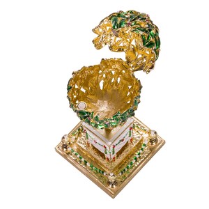 May include: A gold-tone Christmas ornament shaped like a holly wreath with red berries. The ornament is open and has a white interior. The ornament is on a gold-tone stand with a white base.