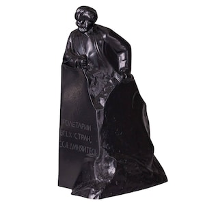 May include: Black and white statue of a man standing on a rock. The man is holding a hammer and chisel. The inscription on the rock reads "Proletarians of all countries, unite!"