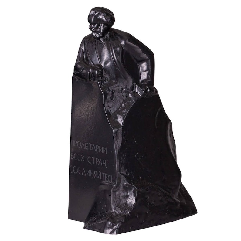 May include: Black and white statue of a man standing on a rock. The man is holding a hammer and chisel. The inscription on the rock reads "Proletarians of all countries, unite!"