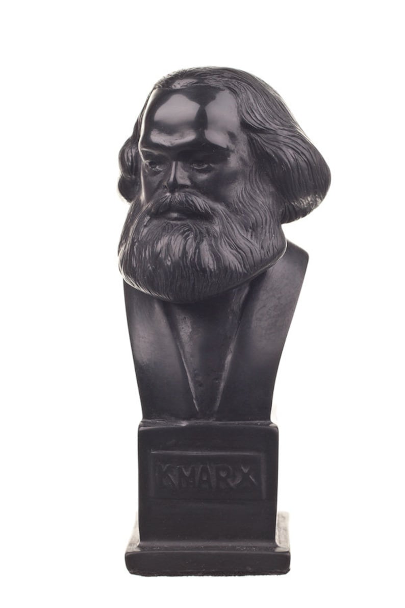 Puede incluir: Un busto de escultura negra de Karl Marx sobre una base negra con la palabra "KMARX" inscrita en la parte delantera.