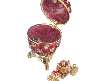 May include: A red and gold jeweled egg with a hinged lid opens to reveal a small, red and gold carriage with wheels. The egg sits on a gold stand with three legs.