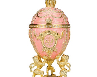 Op de afbeelding: Een roze en gouden Fabergé-ei met een kroon bovenop en twee gouden leeuwen op de basis.