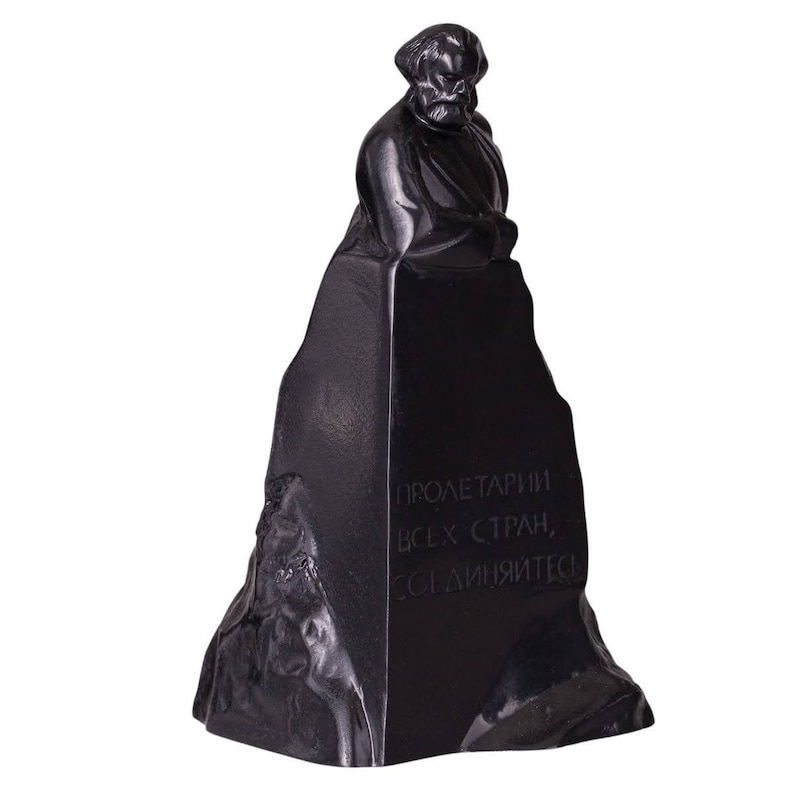 May include: Black and white sculpture of a man with a beard, standing on a pedestal with the inscription "Proletarians of all countries, unite!"
