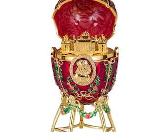 May include: A red and gold Fabergé egg with a detailed miniature building inside. The egg is decorated with floral designs and has a gold stand.