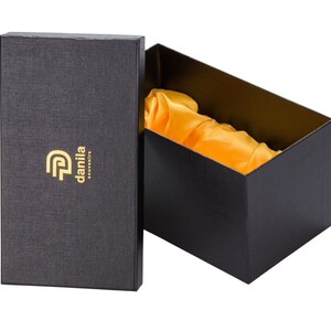 May include: Black gift box with a gold logo that says "danila souvenirs". The box is open and lined with yellow satin.