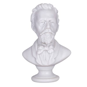 May include: White marble bust sculpture of a man with a beard and bow tie. The bust is on a white pedestal.