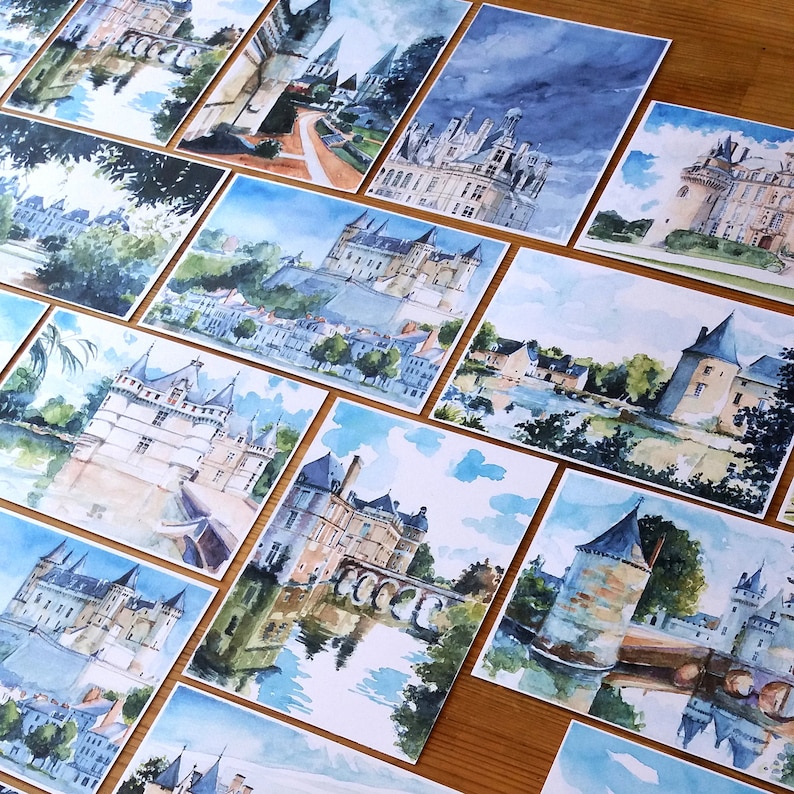 May include: A collection of watercolor paintings depicting various castles and buildings. The paintings are framed and displayed on a wooden surface. The paintings are all in a similar style, with a focus on detail and realism.