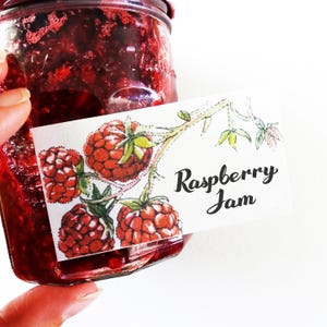 May include: A glass jar filled with red raspberry jam, with a white label that says "Raspberry Jam" and features a watercolor illustration of raspberries on a vine.