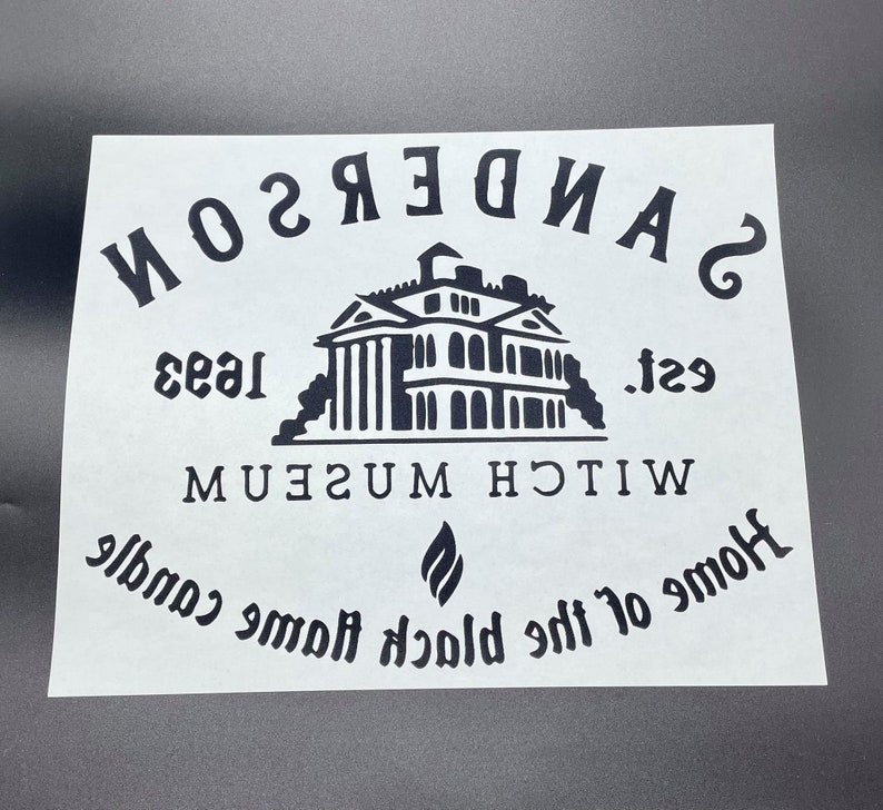 Op de afbeelding: Zwart-wit grafisch ontwerp met de tekst "SANDERSON WITCH MUSEUM est. 1933 Home of the Black Flame Candle" en een silhouet van een huis.