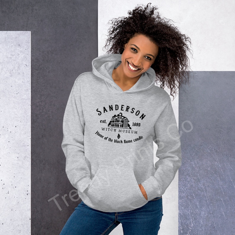 Op de afbeelding: Grijs hoodie met een zwarte grafische print van een huis met de tekst "Sanderson est. 1693 Witch Museum Home of the black flame candle"