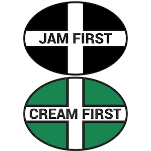 Pode incluir: Dois sinais redondos com uma cruz branca no meio. O sinal superior é preto com o texto "JAM FIRST" em branco. O sinal inferior é verde com o texto "CREAM FIRST" em branco.