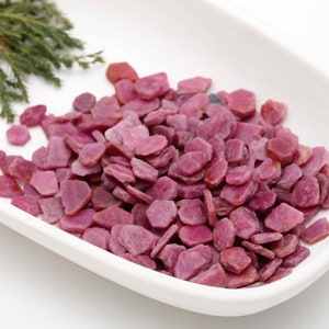 Peut inclure: Un plat en céramique blanche rempli d'une grande quantité de petites pierres précieuses de rubis roses.