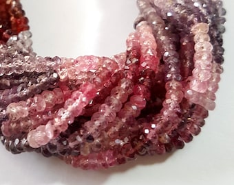 May include: A multi-strand necklace of small, faceted, round beads in a gradient of colors ranging from deep burgundy and dark purple to lighter shades of pink and mauve. The beads are strung together in a dense, twisted arrangement.