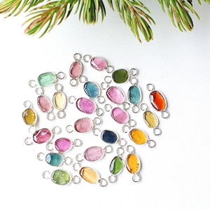 Peut inclure: Un ensemble de 20 breloques connecteurs ovales en pierres précieuses avec des anneaux de saut en argent. Les pierres précieuses sont de différentes couleurs, notamment le rose, le vert, le bleu, le jaune et l'orange.