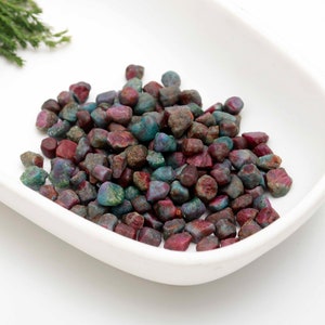 Könnte beinhalten: Eine weiße Schale gefüllt mit einer großen Menge kleiner, roher, roter, grüner und blauer Edelsteine.