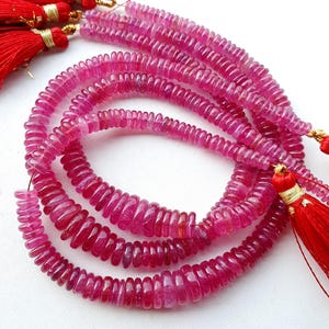 May include: Strands of pink ruby gemstone beads. The beads are disc-shaped and strung together, with red tassels at the ends. The gemstones have a polished, translucent appearance.