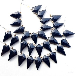 May include: Strands of faceted, black gemstone beads. Each bead is a dark, triangular shape with multiple facets, strung together with gold-colored accents. The beads are displayed against a white background, highlighting their glossy finish.