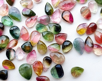 May include: A collection of polished tourmaline gemstones in various shapes and colors, including pink, green, yellow, and clear. The gemstones are teardrop and oval shaped, with a translucent appearance.