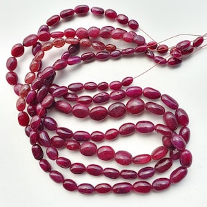 Peut inclure: Plusieurs brins de perles de rubis ovales polies, de nuances de rouge et de bordeaux. Les perles sont enfilées, mettant en valeur leurs variations de couleur naturelles et leurs surfaces lisses. Idéal pour la création de bijoux.