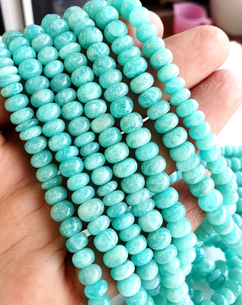 Puede incluir: Una hebra de cuentas de piedras preciosas de color verde turquesa. Las cuentas son redondas y lisas, y est&aacute;n enhebradas en un hilo transparente. Las cuentas est&aacute;n dispuestas en una pila suelta, y est&aacute;n iluminadas por una luz brillante.