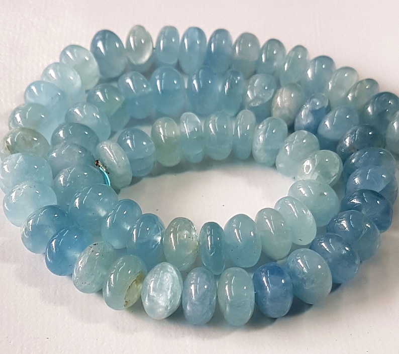 May include: A strand of light blue aquamarine gemstone beads. The beads are smooth and oval shaped.