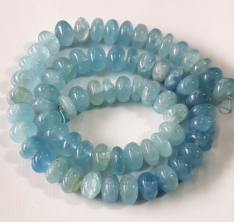 May include: A strand of light blue aquamarine gemstone beads. The beads are oval shaped and have a smooth, polished finish.