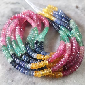 May include: A close-up of a multi-coloured gemstone bead strand. The strand is made up of pink, green, blue, and yellow beads. The beads are all faceted and have a high polish.