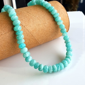 Puede incluir: Un brazalete de cuentas azul turquesa hecho de piedras redondas y lisas. El brazalete est&aacute; sobre un tubo de cart&oacute;n marr&oacute;n.