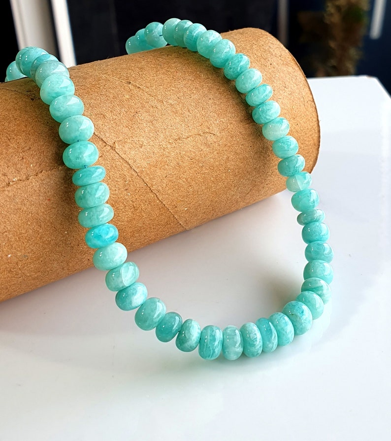 Puede incluir: Un brazalete de cuentas azul turquesa hecho de piedras redondas y lisas. El brazalete est&aacute; sobre un tubo de cart&oacute;n marr&oacute;n.