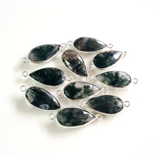 May include: Ten green moss agate teardrop shaped gemstone beads with silver jump rings. The beads are approximately 20mm long and 15mm wide.