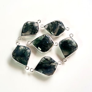 May include: Six green moss agate gemstone pendants with silver bail connectors. The pendants are in the shape of a teardrop with a flat back.