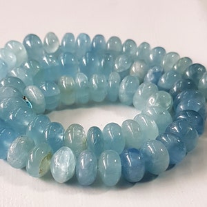 May include: A strand of light blue aquamarine gemstone beads. The beads are smooth and round, with a slightly flattened shape. They are strung on a clear thread.