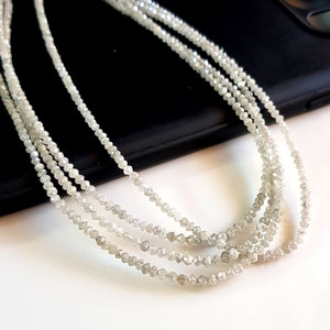 May include: A strand of white rough diamonds, also known as raw diamonds, strung on a thread. The diamonds are small and have a natural, unpolished look.