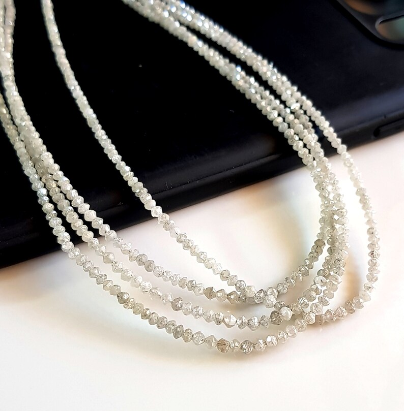 May include: A strand of white rough diamonds, also known as raw diamonds, strung on a thread. The diamonds are small and have a natural, unpolished look.