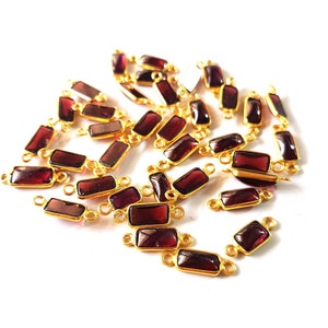 May include: A pile of gold-plated rectangular connectors with red gemstone accents. The connectors have two loops on each side, allowing them to be linked together.