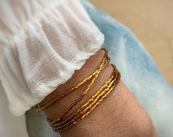 May include: A gold beaded bracelet with multiple strands. The bracelet is made of small, square-shaped beads.