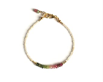 May include: A delicate bracelet featuring a thin gold chain interspersed with small, clear beads and a section of multi-coloured, faceted gemstone rondelles transitioning from green to pink. It includes a gold lobster clasp and a small dangling charm.