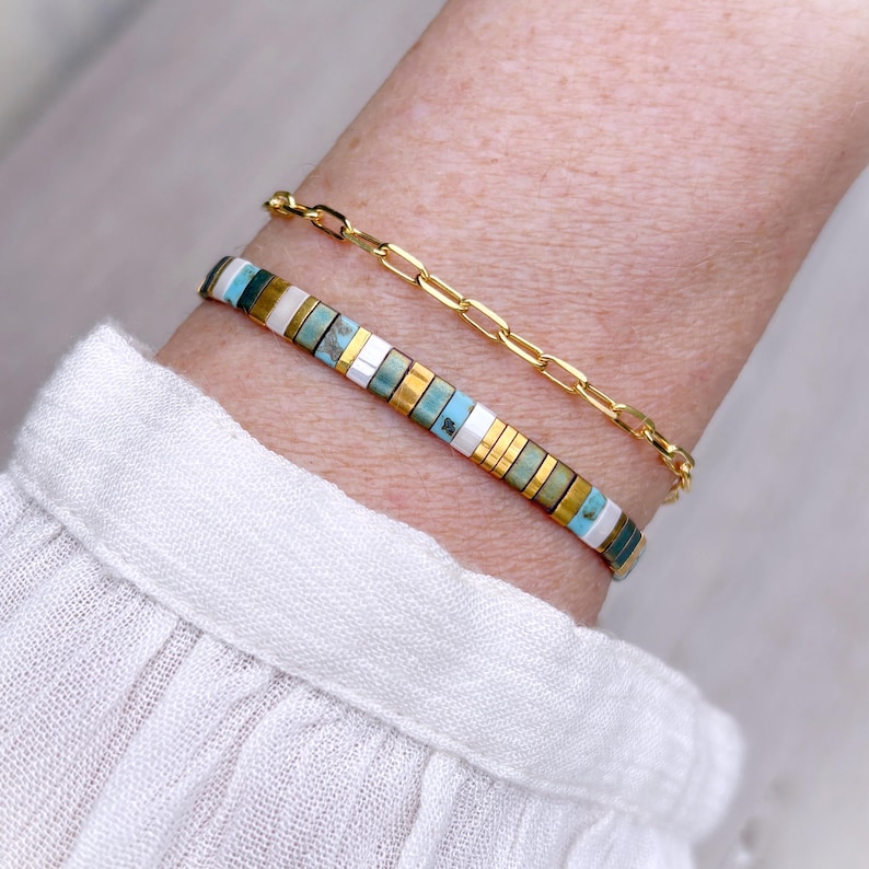 May include: A set of two bracelets consisting of one gold-toned chain link bracelet and one beaded bracelet featuring small rectangular tiles in alternating colors of turquoise, white, metallic gold, and muted green arranged in a repeating pattern.