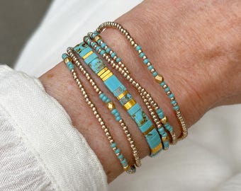 Puede incluir: Un conjunto de pulseras de múltiples hilos que presenta una combinación de pequeñas cuentas metálicas en tono dorado y cuentas planas rectangulares de color turquesa con vetas marrones. El diseño incluye segmentos alternos de espaciadores dorados.