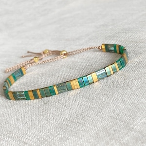 Op de afbeelding: Een groene en gouden kralen armband met een koordsluiting.