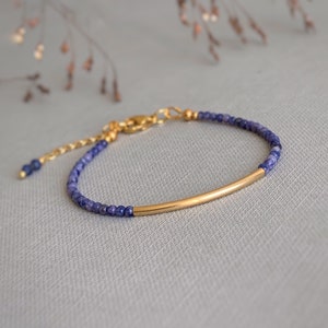 Puede incluir: Una pulsera delicada con peque&ntilde;as cuentas facetadas de color azul oscuro y una pieza central de tubo de metal dorado curvado. La pulsera incluye una cadena extensora de metal dorado con un cierre de mosquet&oacute;n y una cuenta azul al final.