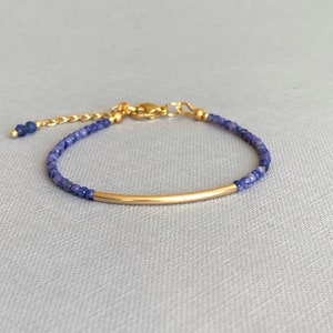 Puede incluir: Una pulsera delicada con peque&ntilde;as cuentas facetadas de color azul oscuro ensartadas en un cord&oacute;n fino. El dise&ntilde;o incluye un tubo de metal dorado, liso y curvado, centrado entre las cuentas, con un cierre de mosquet&oacute;n dorado y una cadena ajustable.
