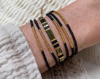 May include: A set of five bracelets stacked on a wrist. The bracelets are made of black and gold beads and a green and black patterned bracelet.