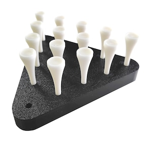 May include: A black, triangular golf tee holder with multiple white golf tees. The holder has a textured surface and a small hole on one side. The tees are arranged in rows, ready for use on the golf course.