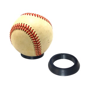 May include: A white baseball with red stitching is displayed on a black plastic stand. A separate black plastic ring is also shown.