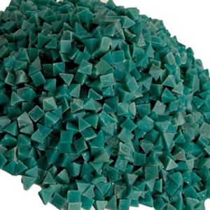 May include: A pile of teal-colored, pyramid-shaped abrasive media. The small, geometric shapes are densely packed together, creating a textured surface. The image is set against a plain white background.