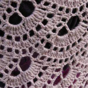 May include: Close-up of a crocheted fabric with a delicate pattern of small holes. The fabric is a light beige color and has a soft, textured appearance.
