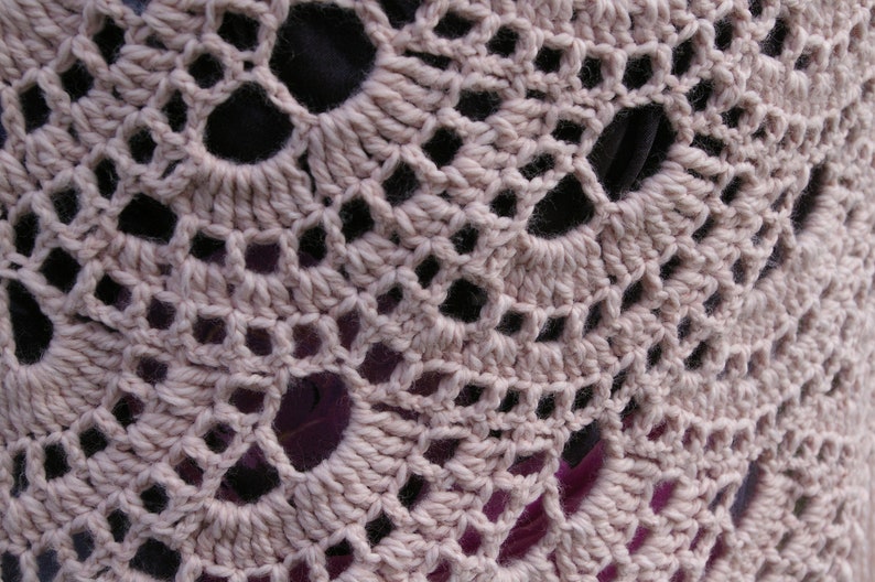 May include: Close-up of a crocheted fabric with a delicate pattern of small holes. The fabric is a light beige color and has a soft, textured appearance.