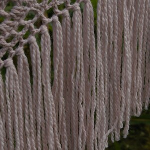 May include: A crocheted shawl with a delicate pattern and long, flowing fringe. The shawl is made of a soft, light pink yarn.