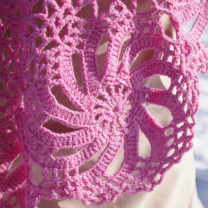 May include: Pink crocheted shawl with a delicate floral pattern. The shawl is made with a fine yarn and has a soft, airy feel.
